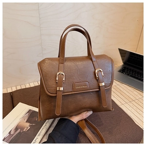 Detail of vintage brown PU leather handbag featuring gold buckles and fine textured finish