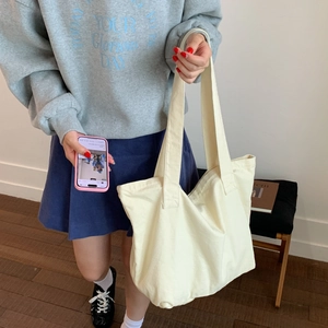 Cream canvas tote bag shown on a model in a minimalist modern interior setting