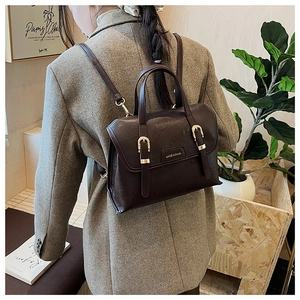 Detail of dark brown vintage backpack with gold buckles worn over a grey blazer