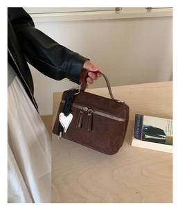 Détail d'un mini sac carré en daim marron avec double fermeture éclair et pendentif cœur