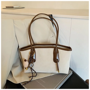 Close-up of cream tote bag with brown leather trim and plush pompom charm detailing
