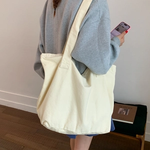 Detailed back view of a person carrying a cream canvas tote bag with a wide shoulder strap