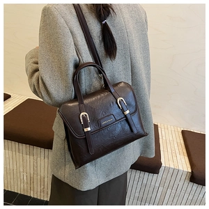 Detail view of a vintage dark brown leather bag with metal buckles and logo plaque