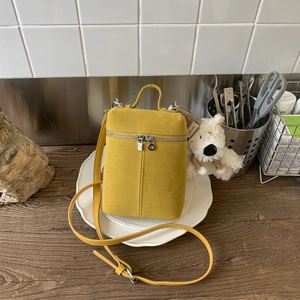 Detail of yellow suede handbag with a plush bear charm and sturdy top handle on a wooden table