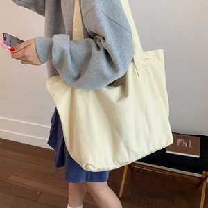 On-shoulder view of a large cream canvas tote bag with wide straps for casual daily style