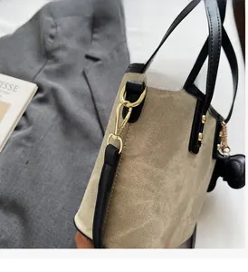 Detail of beige canvas bag with black leather trim, gold hooks, and chic doll pendant