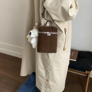 Detail of brown suede bucket bag with plush dog charm and silver zipper on beige coat