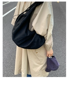 Detail of a large black suede tote bag with drawstring on a woman wearing a trench coat