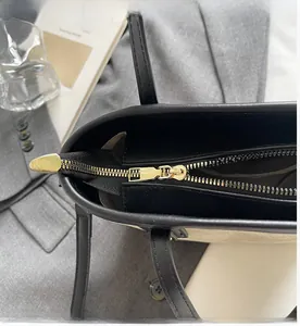 Close-up of smooth gold metal zipper and refined leather texture on black bucket bag