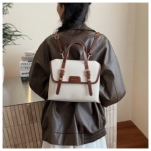 Detail of a vintage-style white and brown leather backpack with gold buckle and brand logo