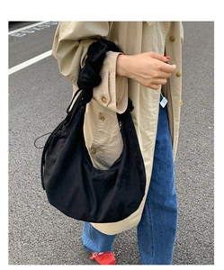 Street view of black suede crescent tote bag with drawstring closure and crossbody strap