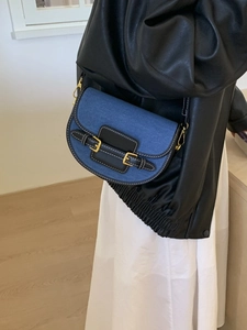 Fashionable denim saddle bag with black leather trim and gold rings worn cross-body
