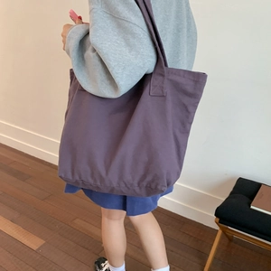 Detailed side view of a large purple canvas tote bag worn by a model in a bright room