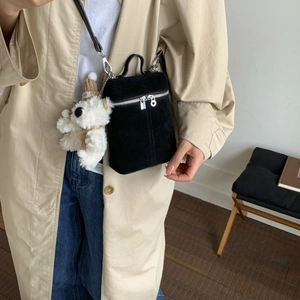 Detail of black suede bucket bag with plush bear charm and crossbody strap styling