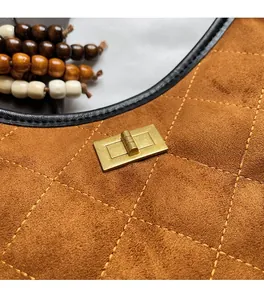 Detail of brown suede shoulder bag featuring quilted stitching and a gold metal twist lock