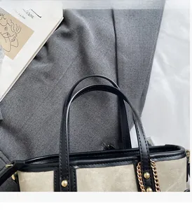Detail of beige canvas tote bag featuring black leather handles and gold metal chain