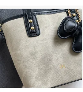 Detail showing the textured canvas fabric, golden logo, and leather bow of the handbag