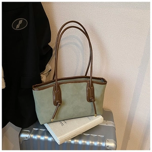 Detail of green suede tote bag with brown leather trim and embossed brand logo