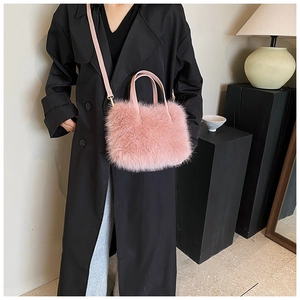 Detail of soft pink faux fur handbag with leather handles worn over a black trench coat