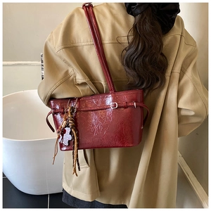 Detail of dark red patent leather shoulder bag with glossy crinkle texture and silver buckle