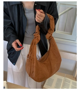 Detailed close-up of brown suede crescent bag with pleated handle and long fringe tassels
