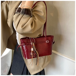 Detail of dark red glossy shoulder bag with leopard print bear charm on beige coat