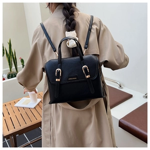 Detail of a vintage black leather backpack with gold buckle worn by a model in a minimal setting