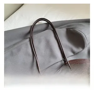 Détails du cabas tressé marron foncé montrant les anses en cuir et boucles dorées