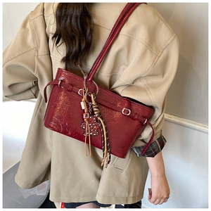 Burgundy patent leather shoulder bag with heart charm and tassel accessory on a model