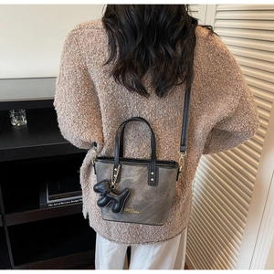 Detail of dark grey bucket bag with black leather straps and a small puppy charm
