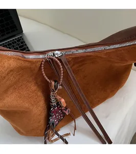 Détail d'un sac cabas en daim marron avec fermeture éclair argentée et breloque léopard