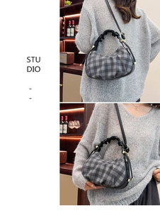 Detail of gray checkered dumpling bag with pleated handle and golden hardware on a model
