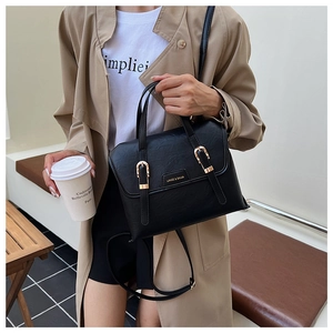 Chic black textured leather handbag with dual gold buckles shown in a city street setting