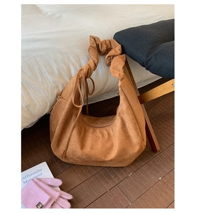 Detail of wide pleated strap and brown suede fabric on crescent shoulder bag