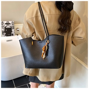 Détail du sac cabas tressé noir avec breloque en perles de bois porté par un modèle