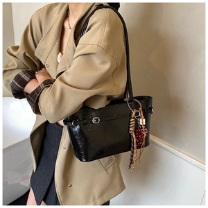 Side view of black glossy leather tote bag with strawberry charm worn by a model