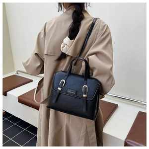 Detail of a vintage black leather crossbody bag with gold buckles and branding worn by a model
