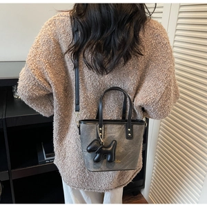 Detailed view of grey textured bucket bag with black leather handle and cute puppy charm
