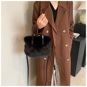 Detail of black faux fur handbag featuring soft plush texture and leather handle on a brown coat