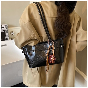 Detail of black crinkled patent leather shoulder bag with bear charm and tassel ornament