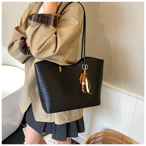 Détail du sac cabas tissé noir avec lanières en cuir et breloque décorative en perles