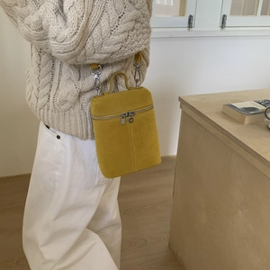 Detail of yellow frosted suede bucket bag with silver hardware and top handle shown on model