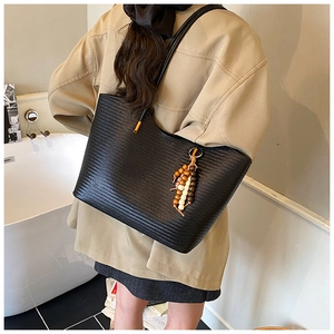 Détail d'un sac cabas noir tressé avec perles décoratives en bois et fines lanières