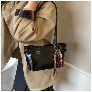 Detail of black glossy tote bag with a decorative leopard bear charm and metal buckle