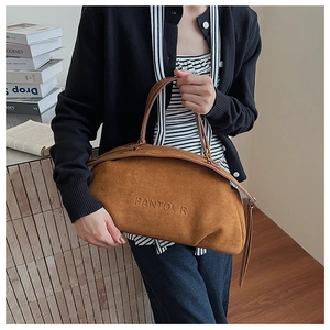 Brown suede satchel bag with embossed logo shown on a model in a minimalist library setting