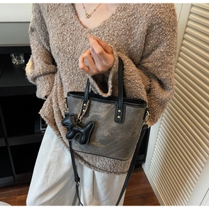 Detail of taupe marble-textured bucket bag with black leather handle and dog-shaped charm
