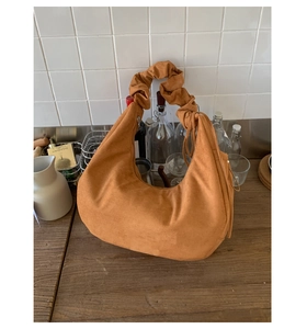 Detail view of caramel brown suede handbag with pleated handles on a wooden tabletop