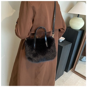 Fashionable black faux fur handbag with leather strap shown on a brown wool coat