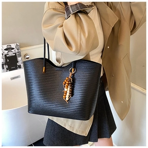 Détail du sac cabas tressé noir avec breloque en perles de bois sur un mannequin
