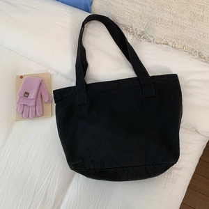 Detail of minimalist black canvas tote bag with wide straps on white bedding background